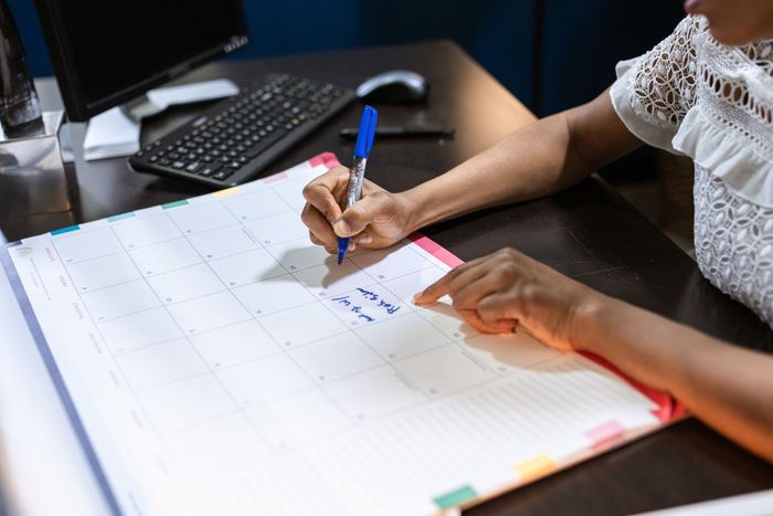 Hands writing on a monthly paper planner at an office desk.